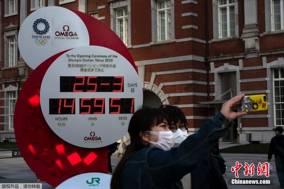 资料图：东京奥运会宣布延期后，行人在更改的计时牌前使用手机拍照合影。