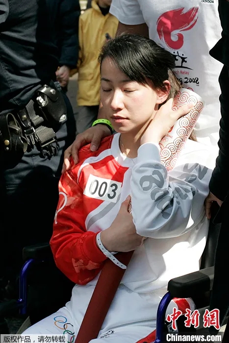 资料图:当地时间2008年4月7日,北京奥运圣火在境外传递时遭遇干扰,中国残奥会击剑运动员金晶坐在轮椅上紧紧保护着熄灭的奥运火炬。 资料图:当地时间2008年4月7日,北京奥运圣火在境外传递时遭遇干扰,中国残奥会击剑运动员金晶坐在轮椅上紧紧保护着熄灭的奥运火炬。