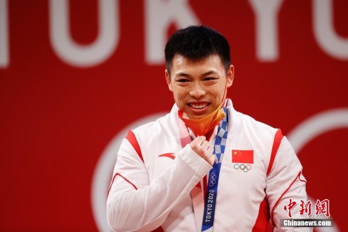 北京时间7月25日晚，在东京奥运会男子举重67公斤级比赛中，中国选手谌利军以抓举145公斤、挺举187公斤、总成绩332公斤夺冠，打破挺举和总成绩奥运纪录的同时，也为中国体育代表团摘得本届奥运会的第六金。图为谌利军在颁奖仪式上摘下口罩。 /p中新社记者 韩海丹 摄