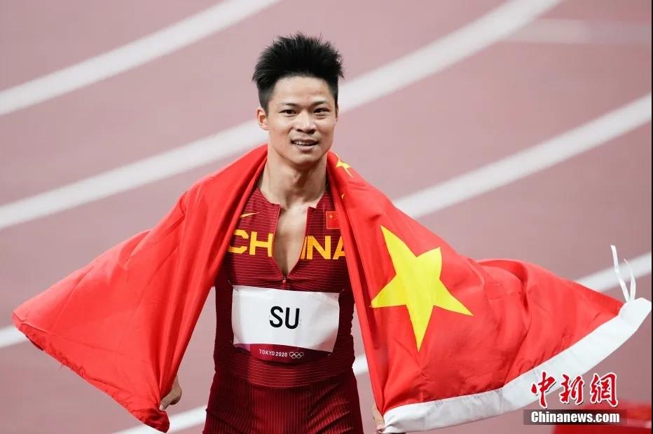当地时间8月1日晚，在东京奥运会男子百米决赛中，中国选手苏炳添以9.98秒的成绩获得第六名，作为首位闯进奥运男子百米决赛的中国人，他再次创造了历史。图为苏炳添在赛后身披国旗。图片来源：视觉中国